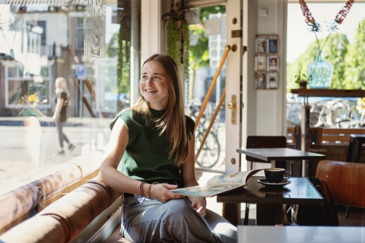 Milou zit op de bank in het café en kijkt lachend naar buiten
